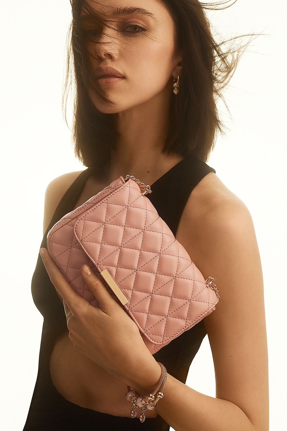 Vaaleanpunainen laukku, jossa on tikattu kuvio ja kullanvärinen olkahihna.