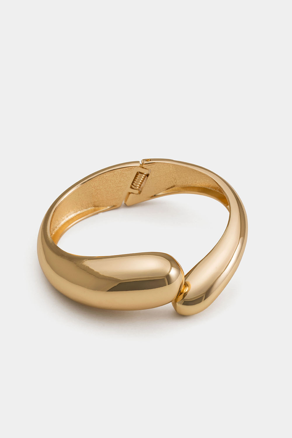 Kullanvärinen leveä rannerengas, jossa on pyöristetyt muodot.