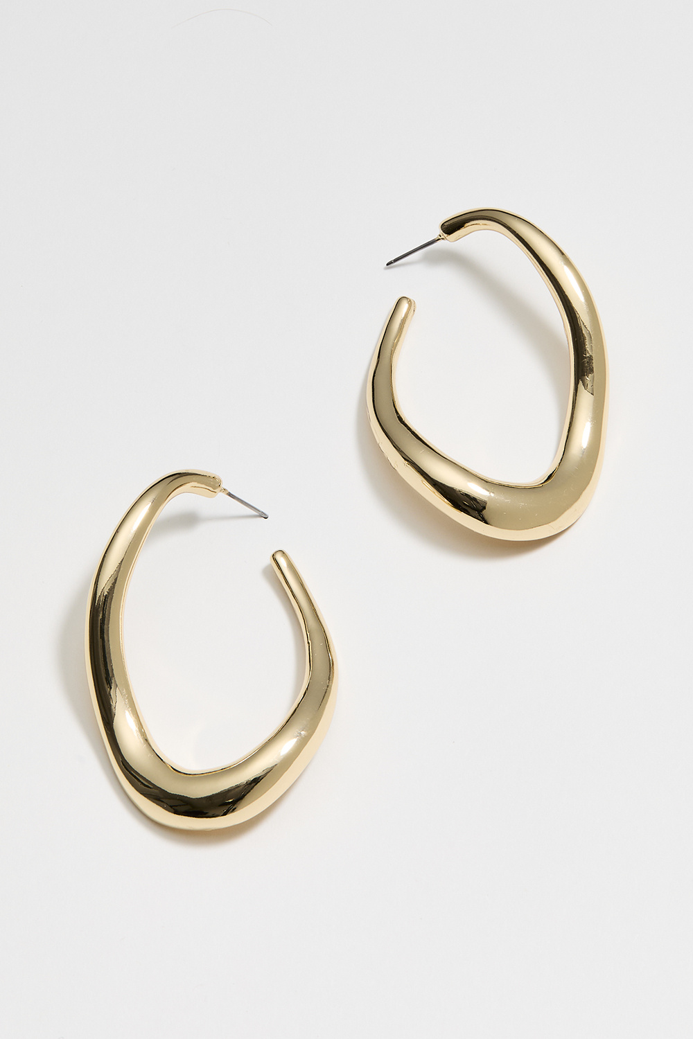 Suuret kullanväriset korvarenkaat, joissa aaltoileva muoto