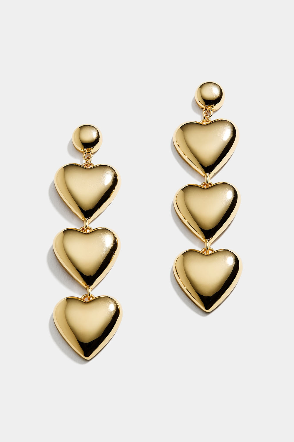 Pitkät kullanväriset korvakorut, joissa kolme sydäntä