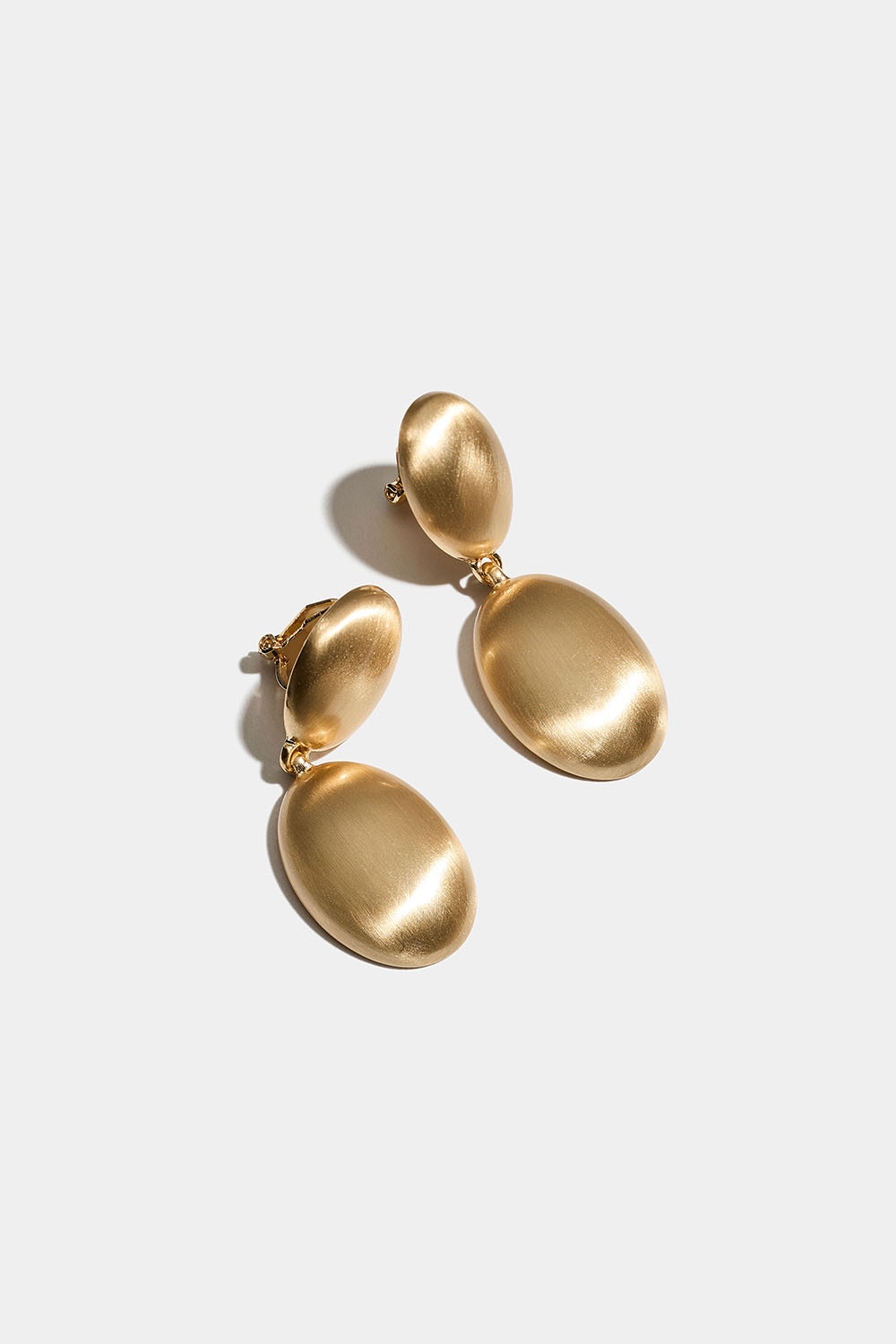 Soikeat kullanväriset klipsikorvakorut, joissa on mattaharjattu muotoilu